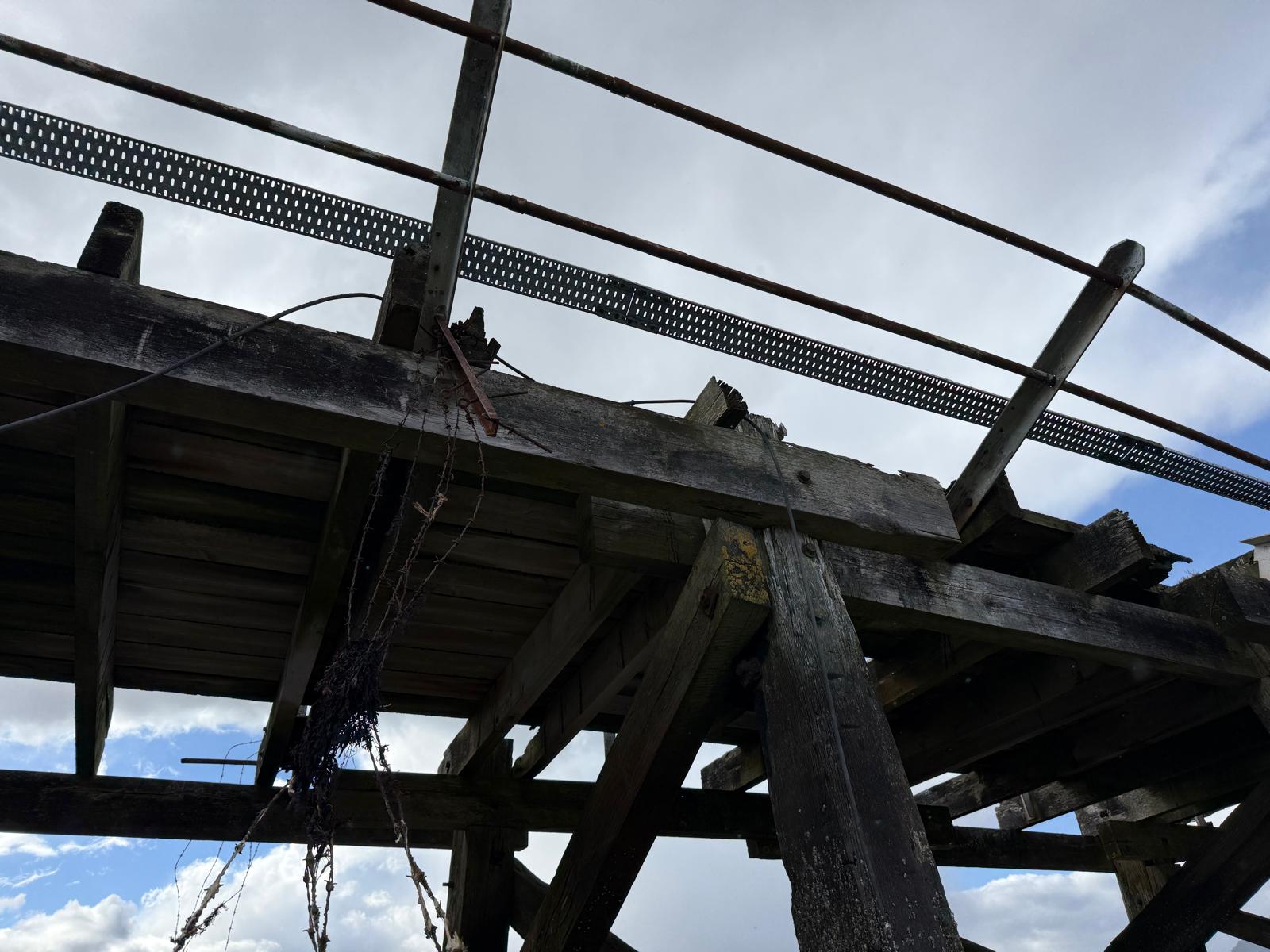 Detail of damaged pier crossbeams with frayed wire and barbed wire fragments tangled around the timbers.